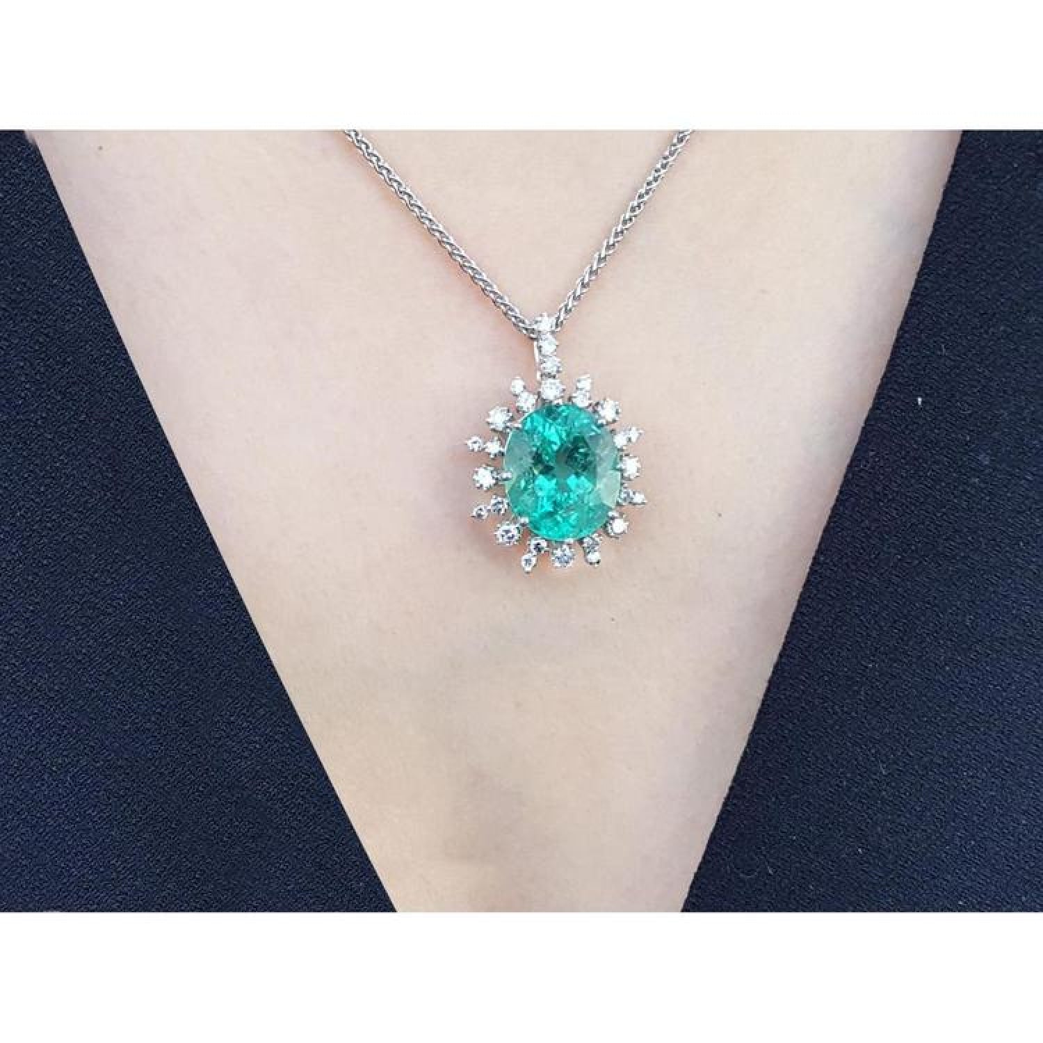 Oval emerald pendant with diamond halo on a 14K white gold chain, worn on a person.