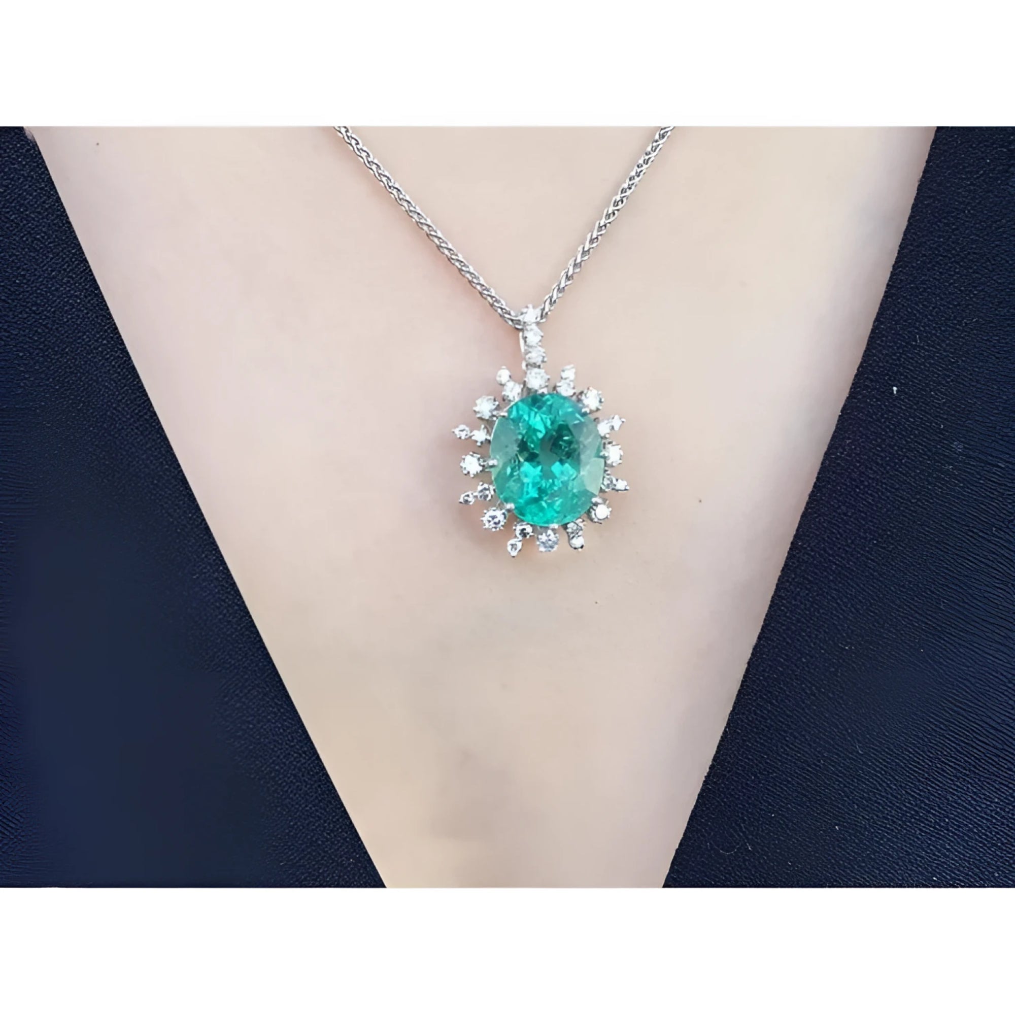 Oval emerald pendant with diamond halo on a 14K white gold chain, worn on a person.