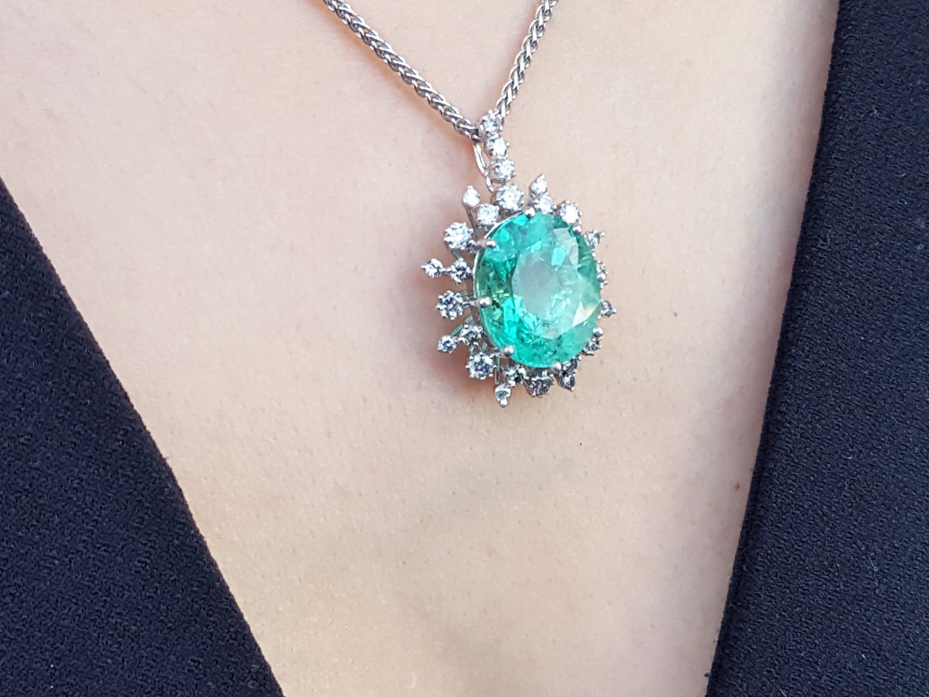 Emerald green gemstone pendant on a chain against a neutral background