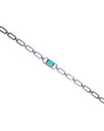 A distant view of a paperclip style bracelet with a natural emerald on a white background.