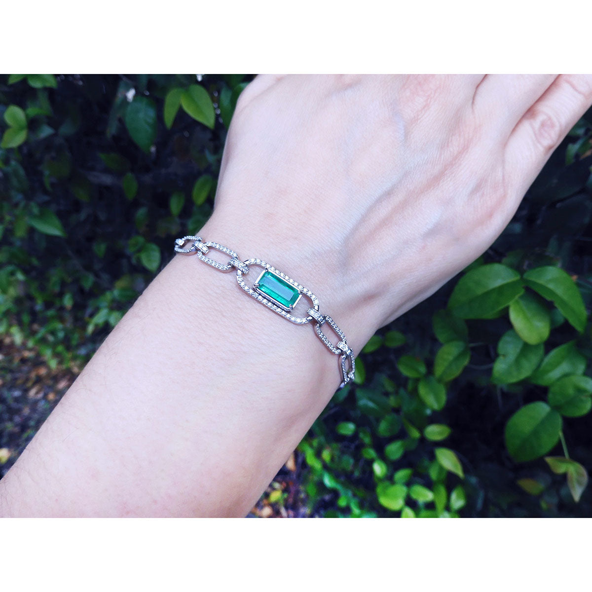 A natural colombian emerald paperclip bracelet on a wrist against a natural background.