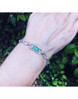 A natural colombian emerald paperclip bracelet on a wrist against a natural background.