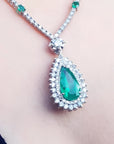 Pear cut emerald necklace with double diamond halo in 18K white gold.