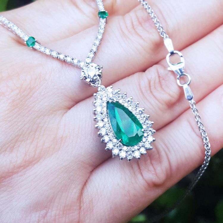 Closer view of a green teardrop emerald pendant with chain held in hand