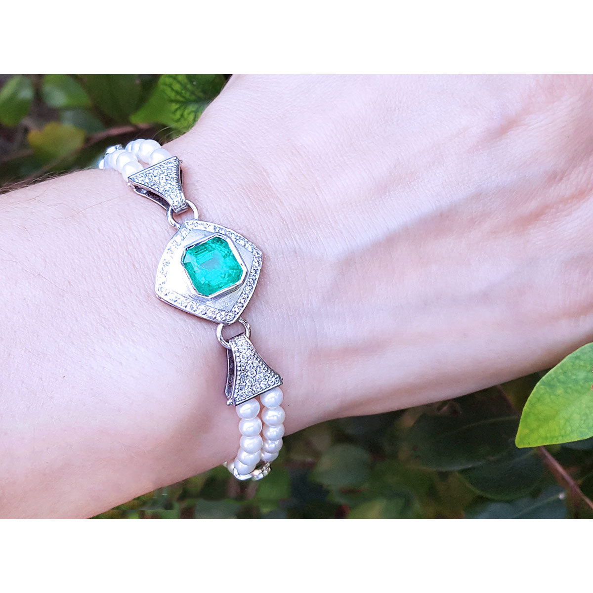 Bracelet with emerald stone and pearl accents on a wrist against a natural background.