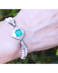 Bracelet with emerald stone and pearl accents on a wrist against a natural background.