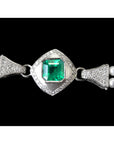 Pearl bracelet with a central emerald stone and white gold clasp on a black background.