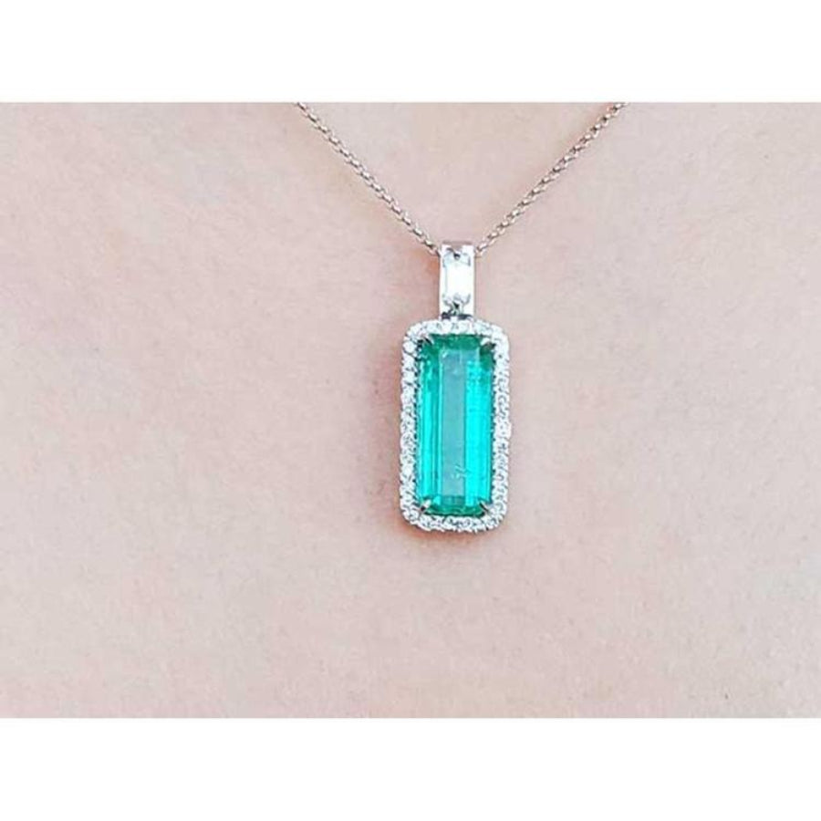 Natural emerald in a halo diamond pendant necklace on a skin pink background.