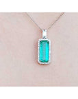 Natural emerald in a halo diamond pendant necklace on a skin pink background.