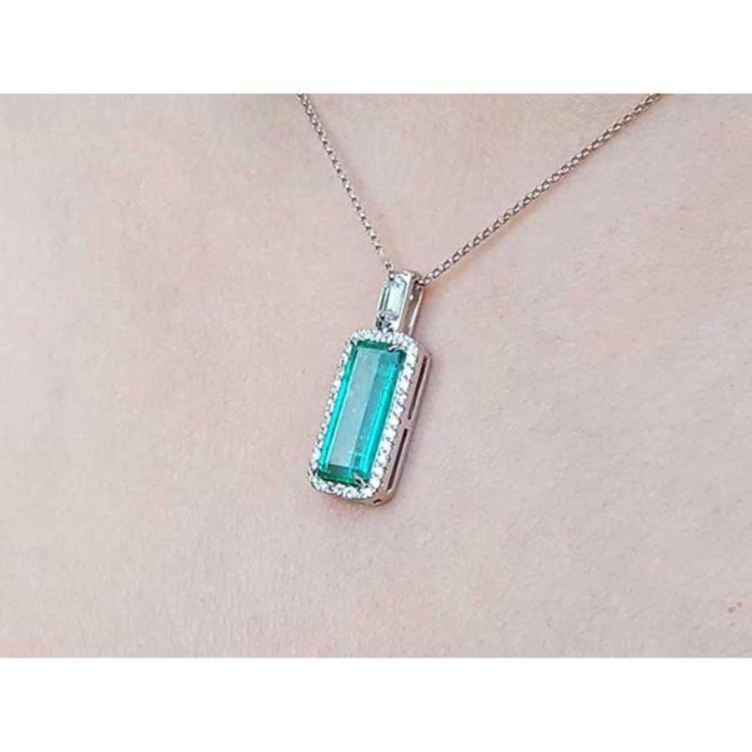 Elongated natural emerald pendant with halo diamonds in 18K white gold on a chain.
