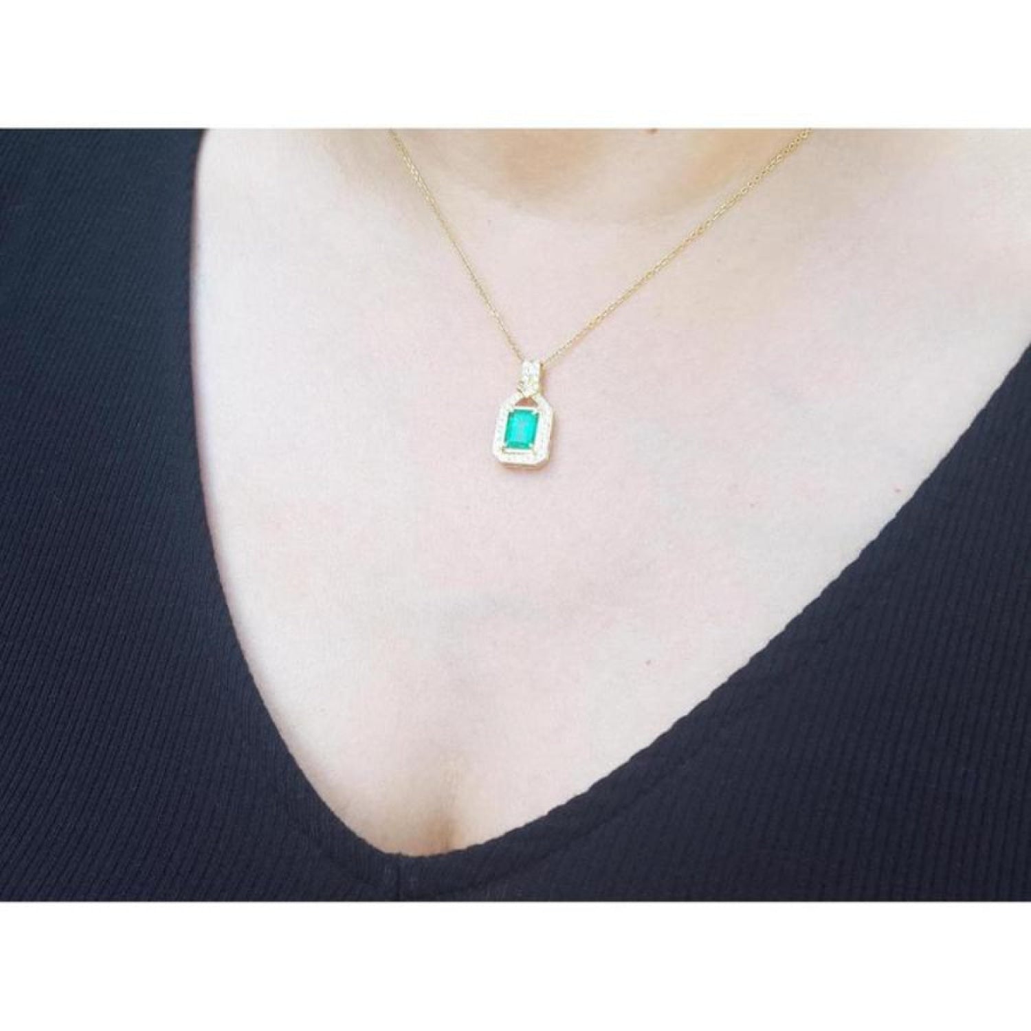 Emerald pendant with natural diamonds on 18K yellow gold chain, worn on a woman's chest.
