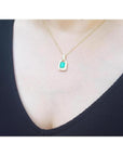 Emerald pendant with natural diamonds on 18K yellow gold chain, worn on a woman's chest.