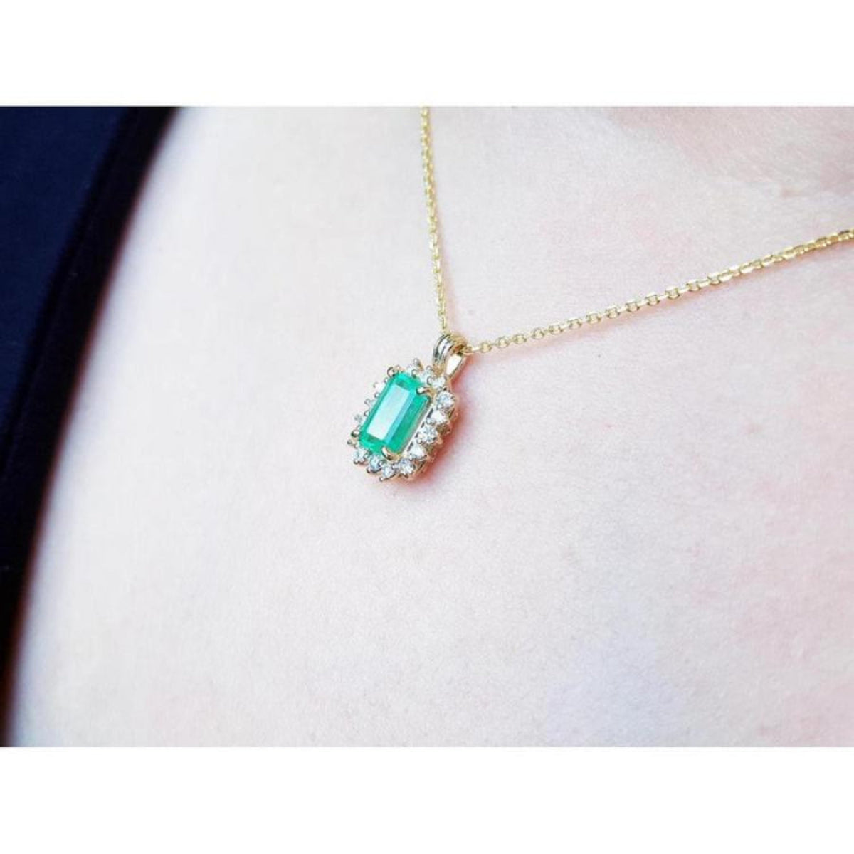 14K yellow gold pendant with a rectangular emerald surrounded by a halo of natural diamonds, worn on a neck.