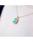 14K yellow gold pendant with a rectangular emerald surrounded by a halo of natural diamonds, worn on a neck.