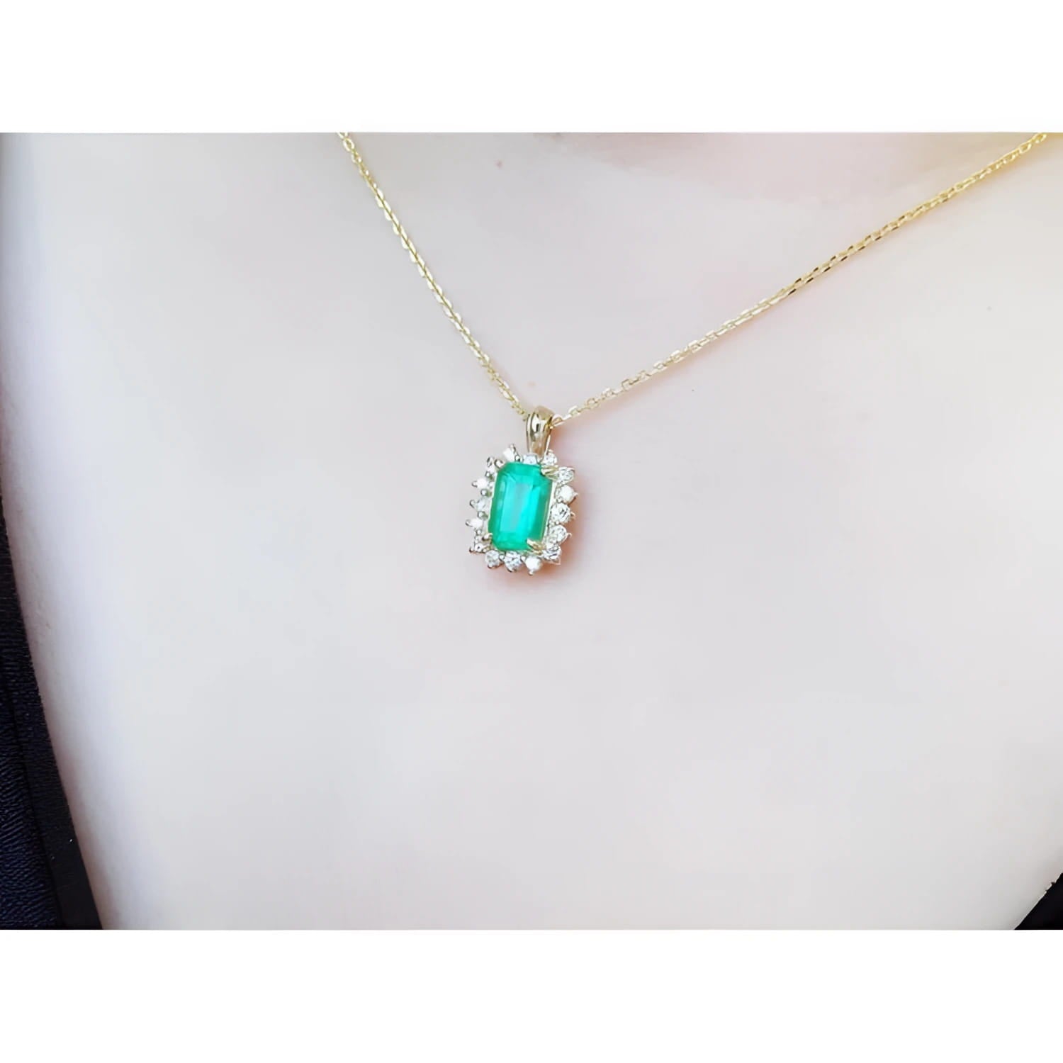 Emerald pendant with a halo of diamonds on a gold chain, worn on a person's chest.