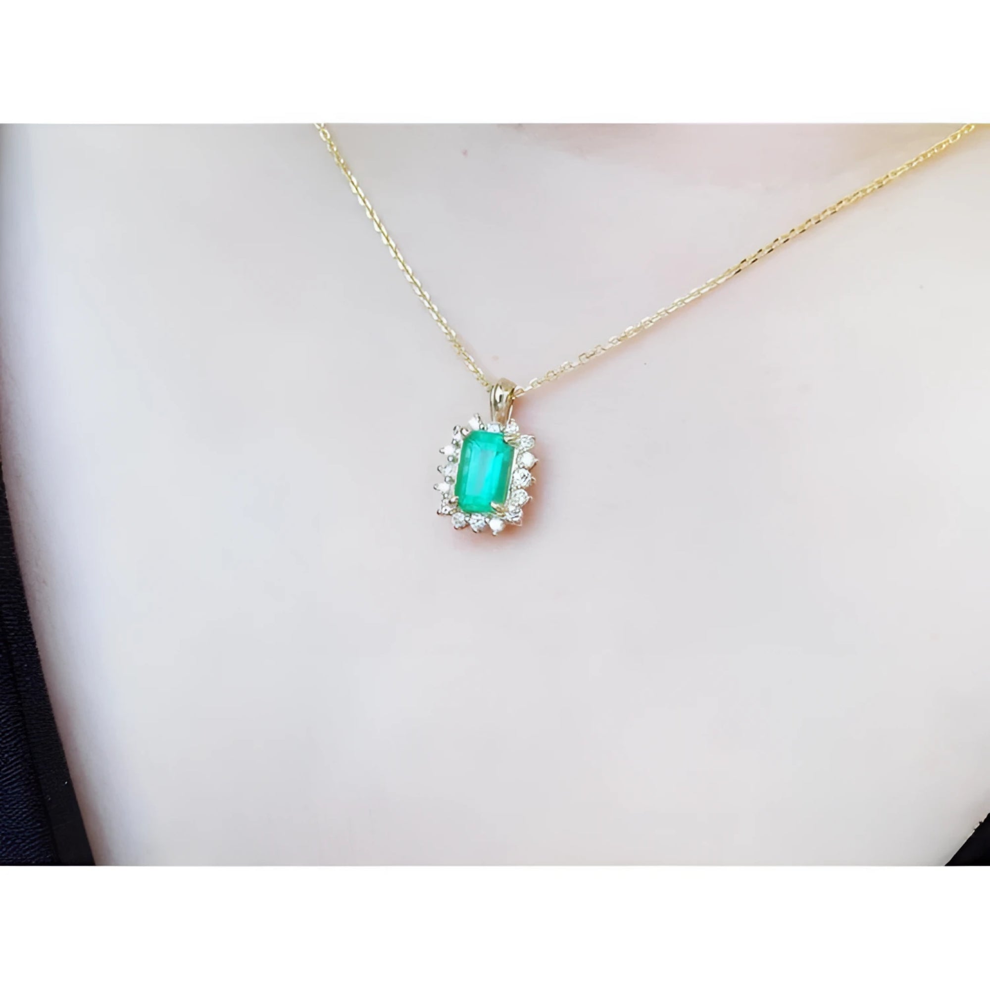 Emerald pendant with a halo of diamonds on a gold chain, worn on a person's chest.