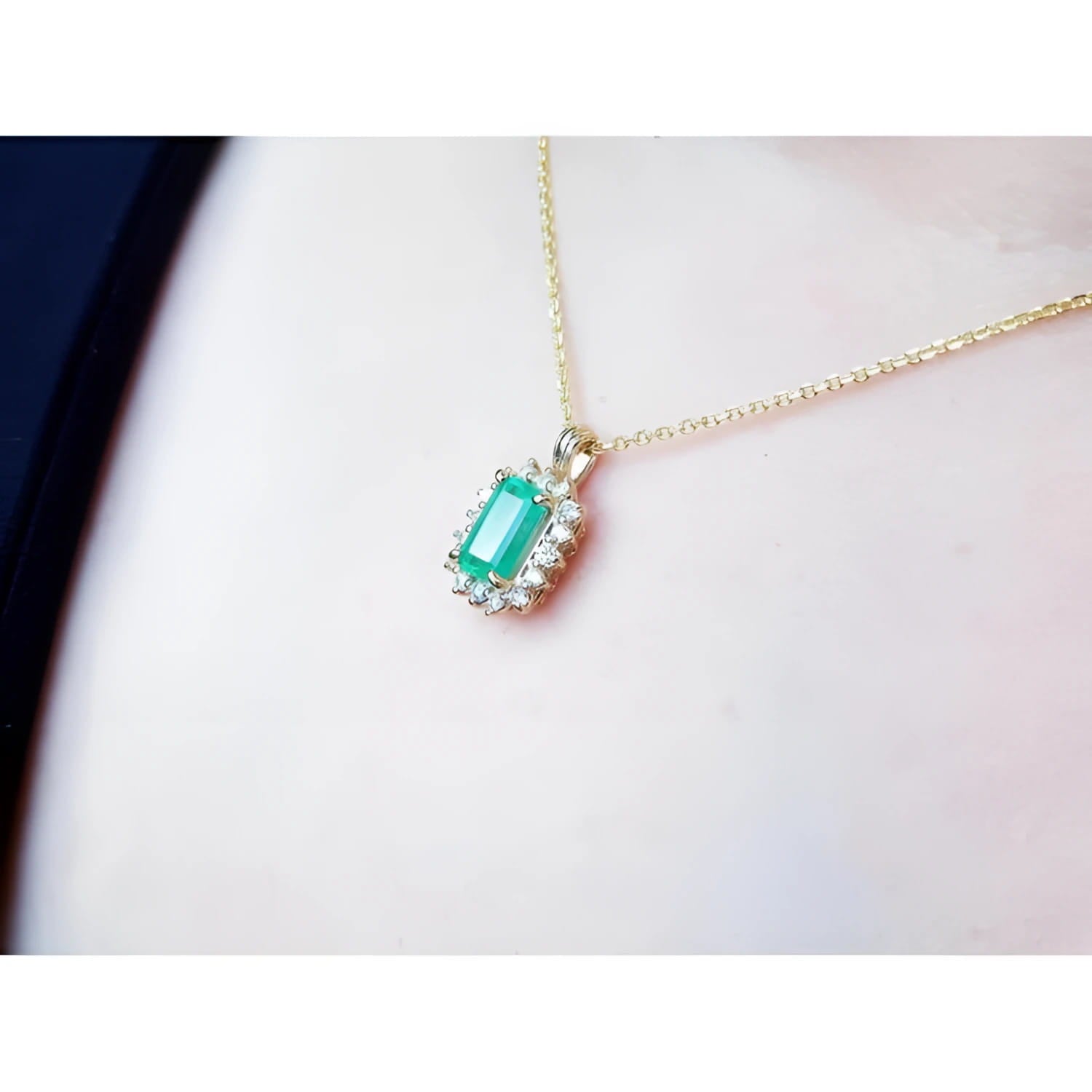 14K yellow gold pendant with a rectangular emerald surrounded by a halo of natural diamonds, worn on a neck.