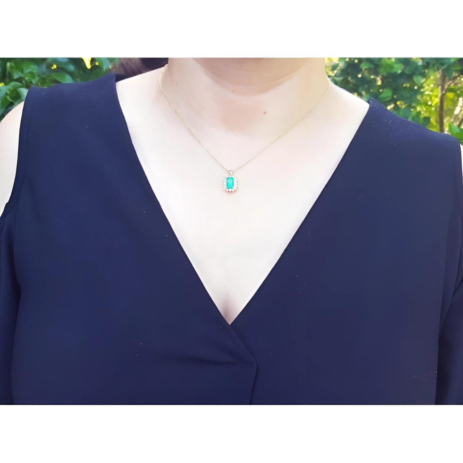 14K yellow gold pendant with a rectangular emerald surrounded by a diamond halo, worn on a woman's neck.