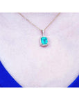 Emerald-cut Colombian emerald pendant with diamond halo on a 14k yellow gold chain, worn on a neck.