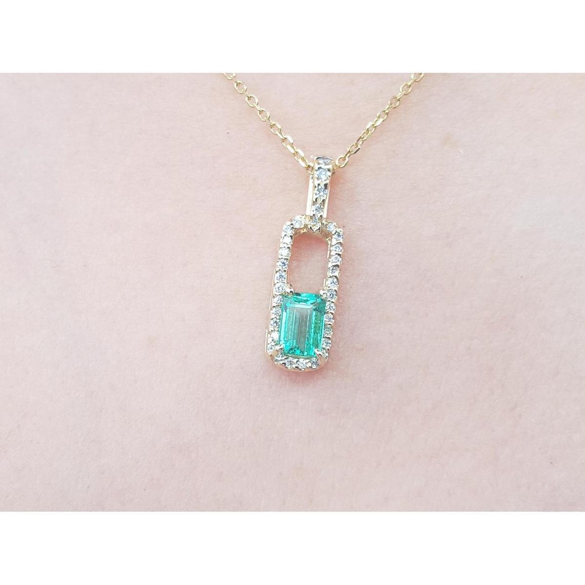 Gold necklace with a colombian emerald pendant on a light pink background.