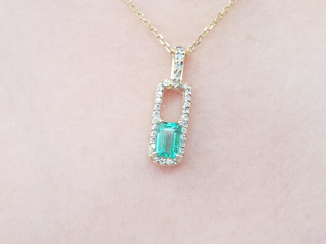 Gold necklace with a colombian emerald pendant on a light pink background.