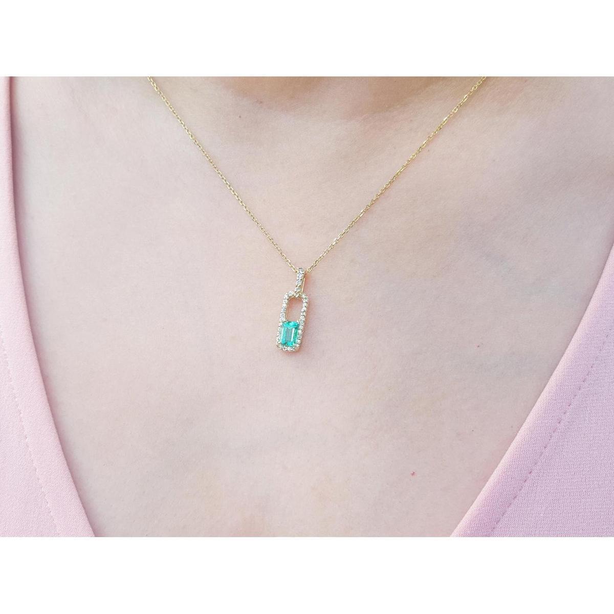 Gold necklace with a real colombian emerald pendant on a person wearing a pink top.