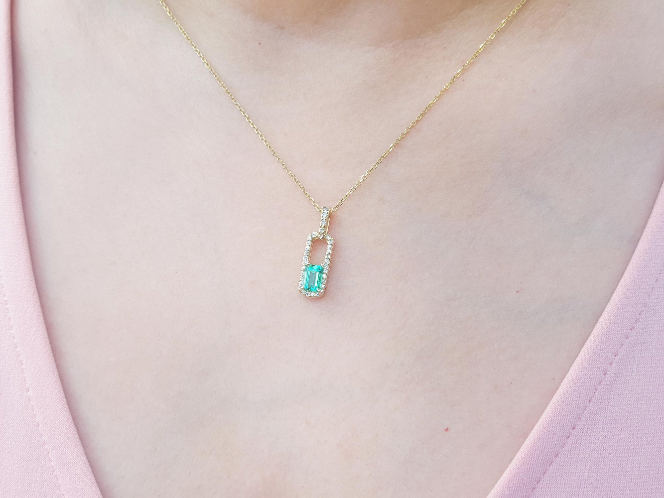 Gold necklace with a real colombian emerald pendant on a person wearing a pink top.