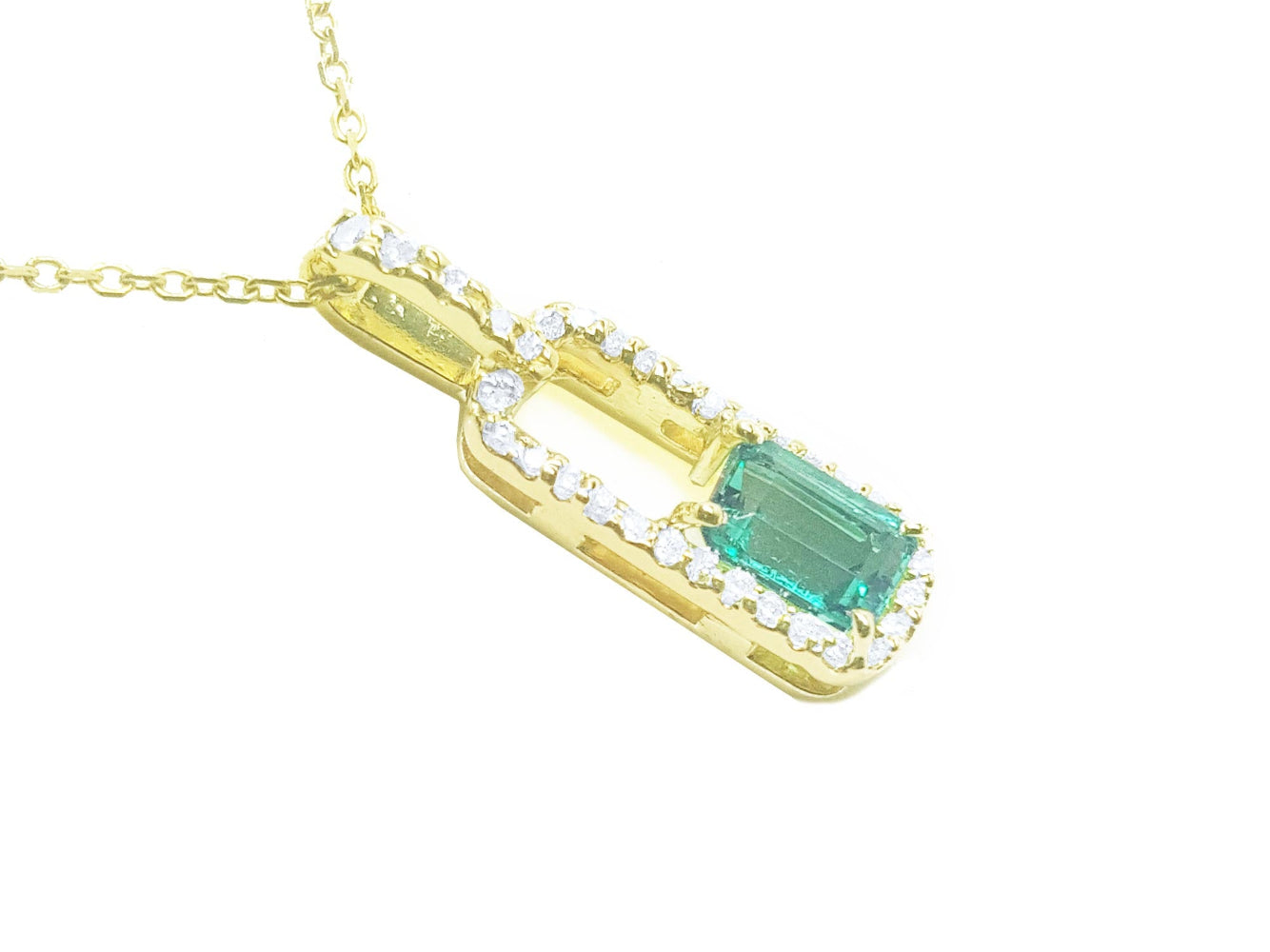 An emerald-cut Colombian emerald pendant with a halo of natural diamonds, handcrafted in 18K yellow gold.