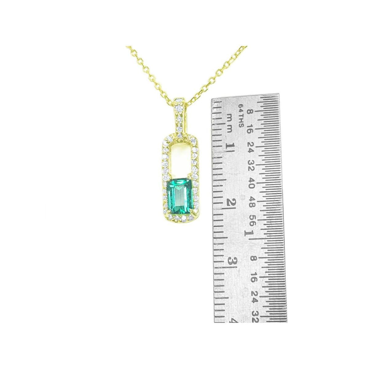 Gold necklace with a natural emerald pendant next to a ruler for size reference on a white background.