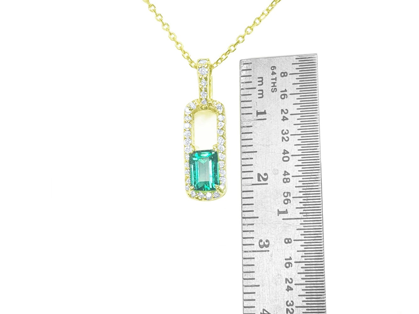 Gold necklace with a natural emerald pendant next to a ruler for size reference on a white background.
