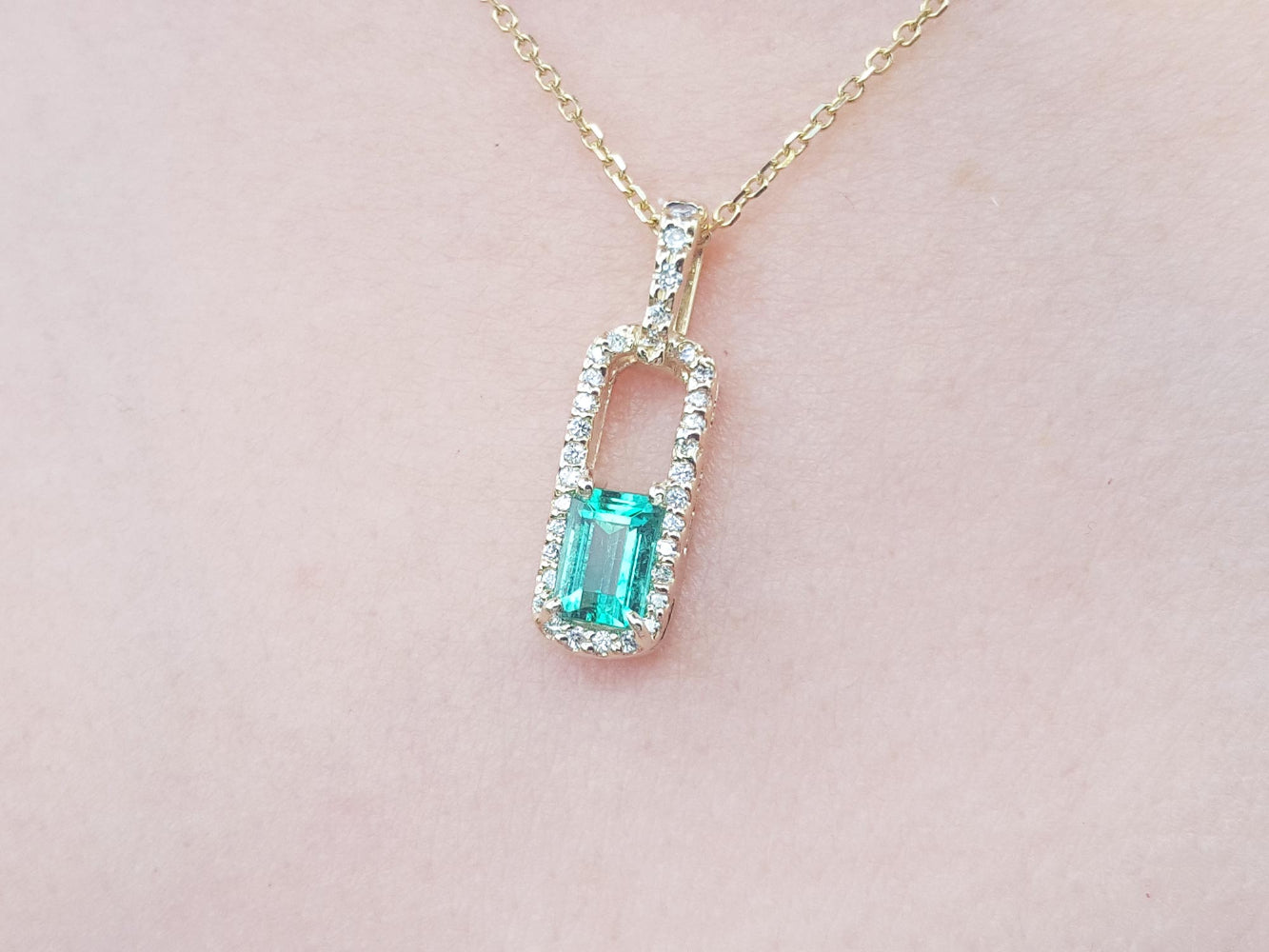 Gold necklace with a natural emerald pendant on a pink skin background.