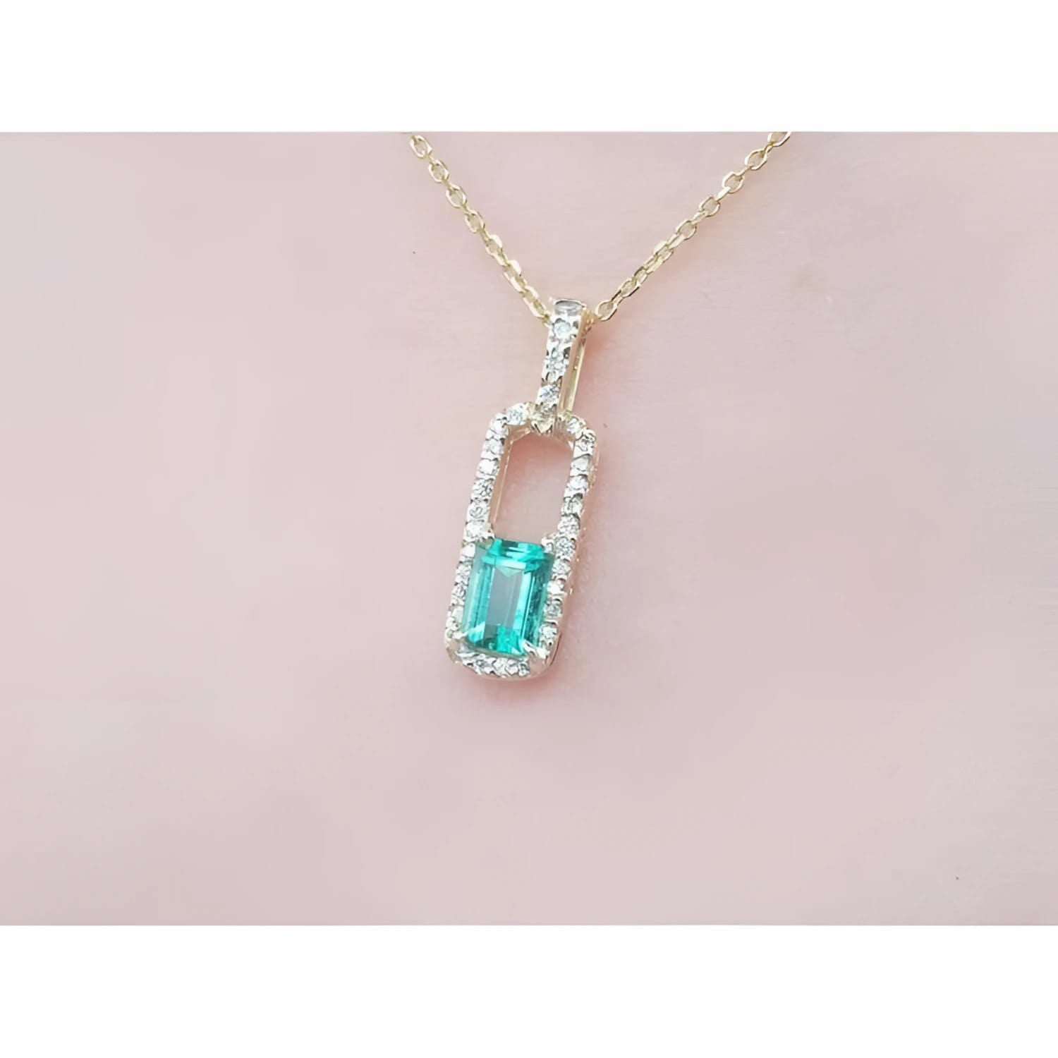Gold necklace with a natural emerald pendant on a pink skin background.