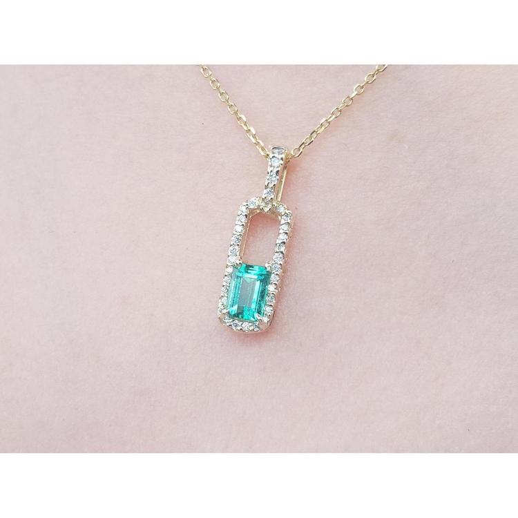 Gold necklace with a natural emerald pendant on a pink skin background.