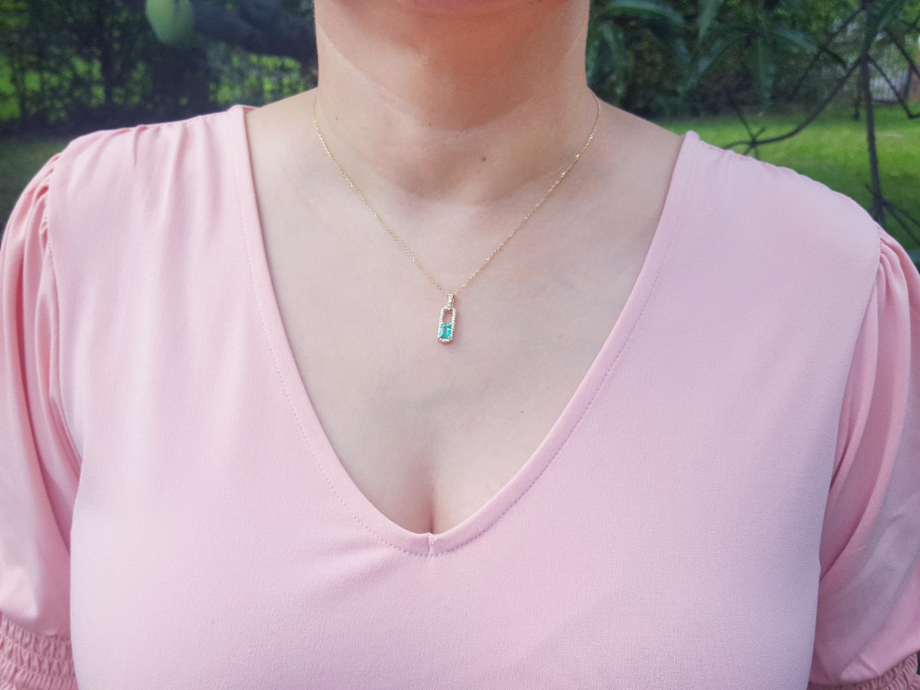Person wearing a pink top with a necklace featuring a natural colombian emerald pendant in outdoors.
