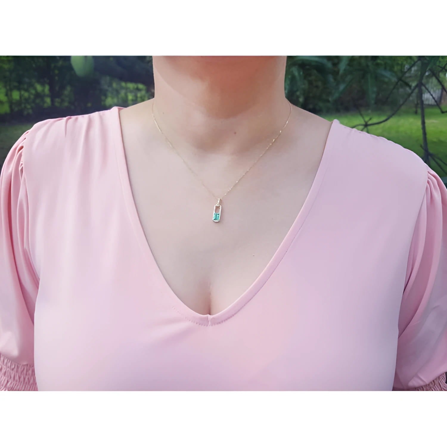 Emerald-cut emerald and diamond halo pendant on an 18K yellow gold chain, worn on a model.