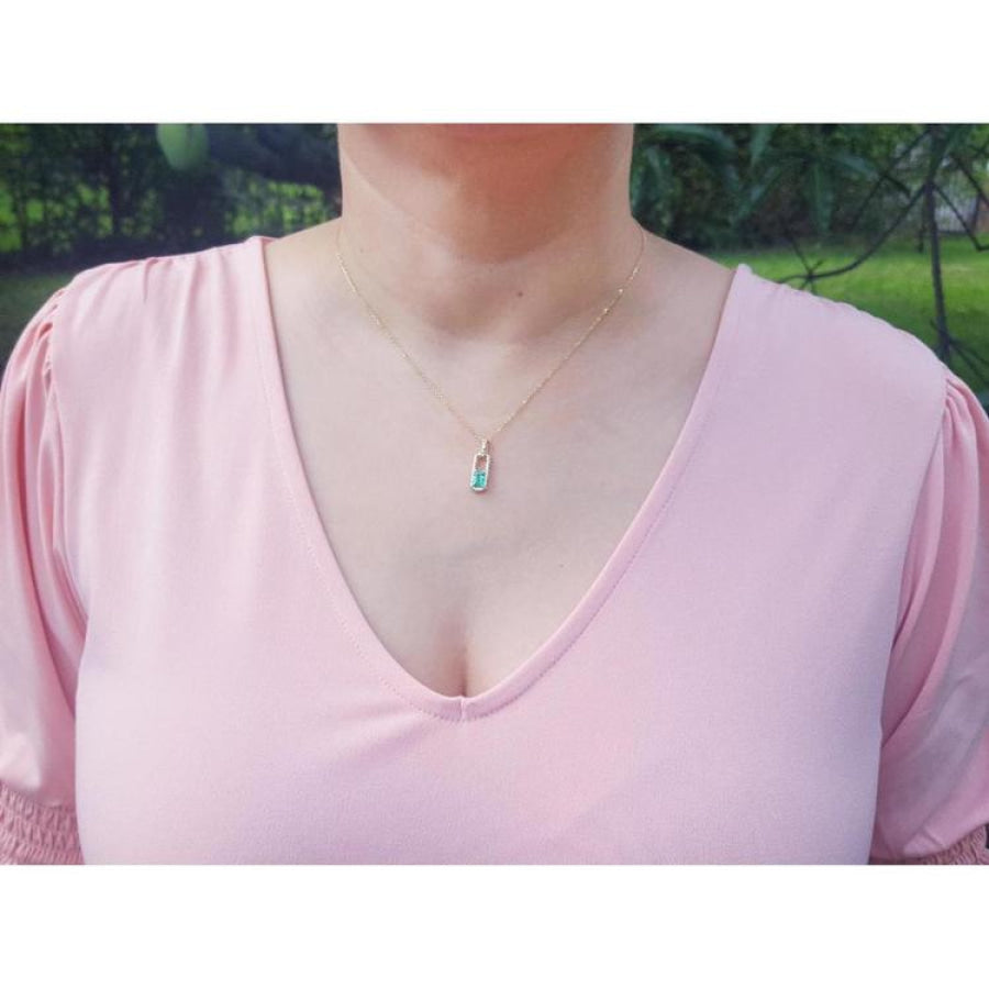 Emerald-cut emerald and diamond halo pendant on an 18K yellow gold chain, worn on a model.
