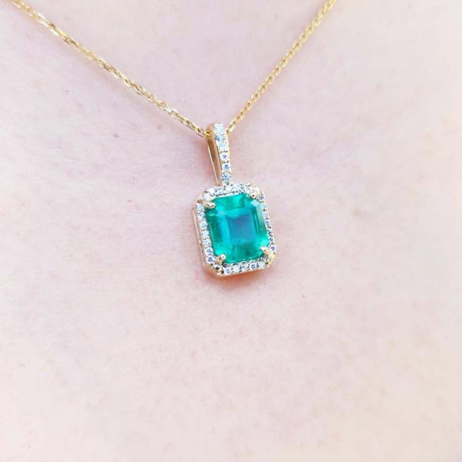 Natural colombian emerald pendant on a gold chain against a light pink skin background.