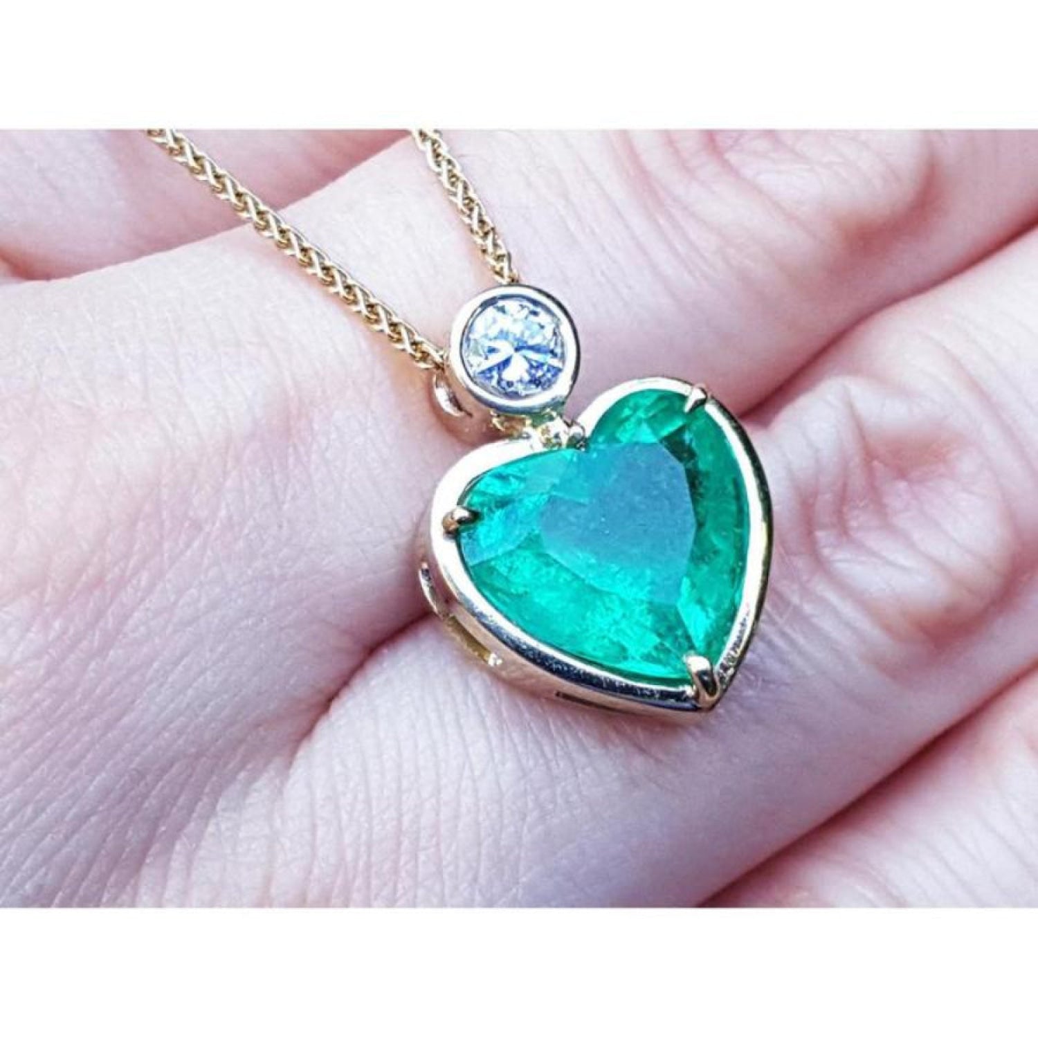 5.46 ct. heart-shaped emerald pendant in 18K yellow gold with a slider bail and bezel-set diamond.