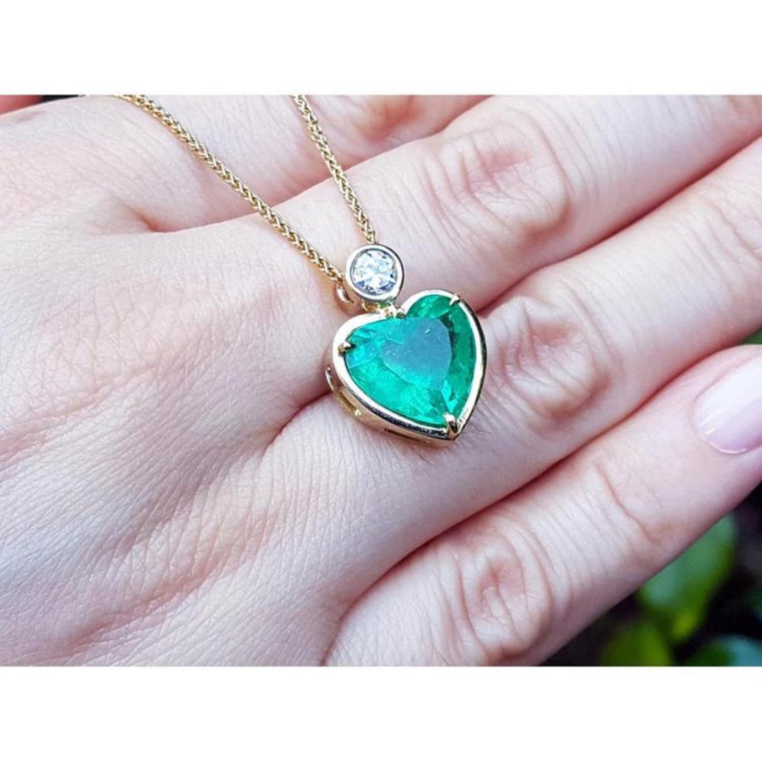 Heart-shaped emerald pendant in 18K yellow gold with a diamond slider bail on a delicate gold chain.