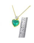 Heart-shaped emerald pendant necklace in 18K yellow gold with a diamond slider bail, shown with a ruler for scale.