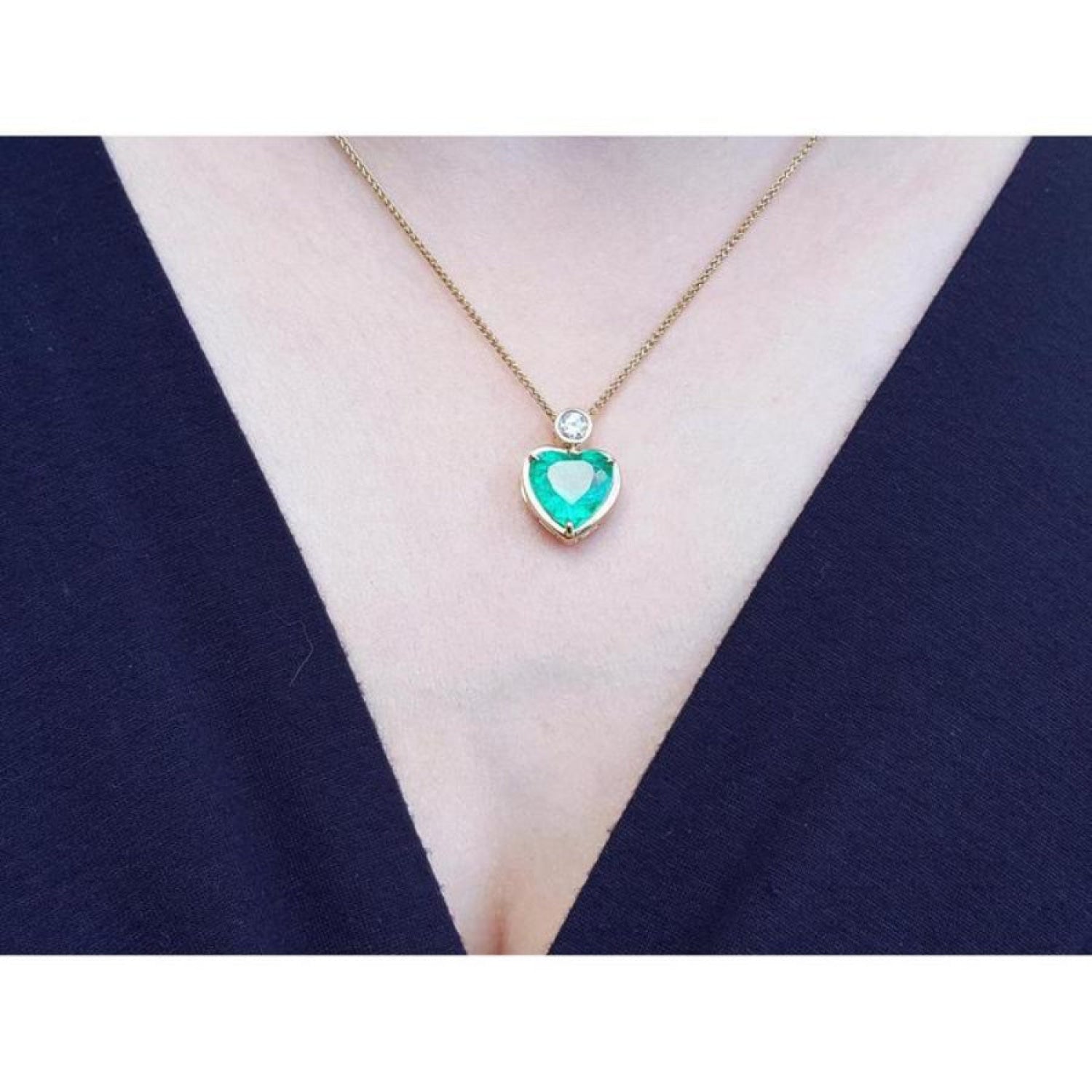Heart-shaped emerald pendant necklace in 18K yellow gold with a diamond accent on a woman's neck.