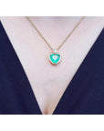 Heart-shaped emerald pendant necklace in 18K yellow gold with a diamond accent on a woman's neck.