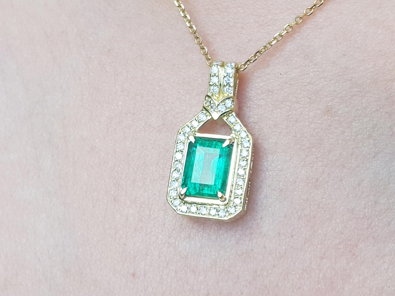 Gold pendant with square natural emerald and diamonds on a pink skin background