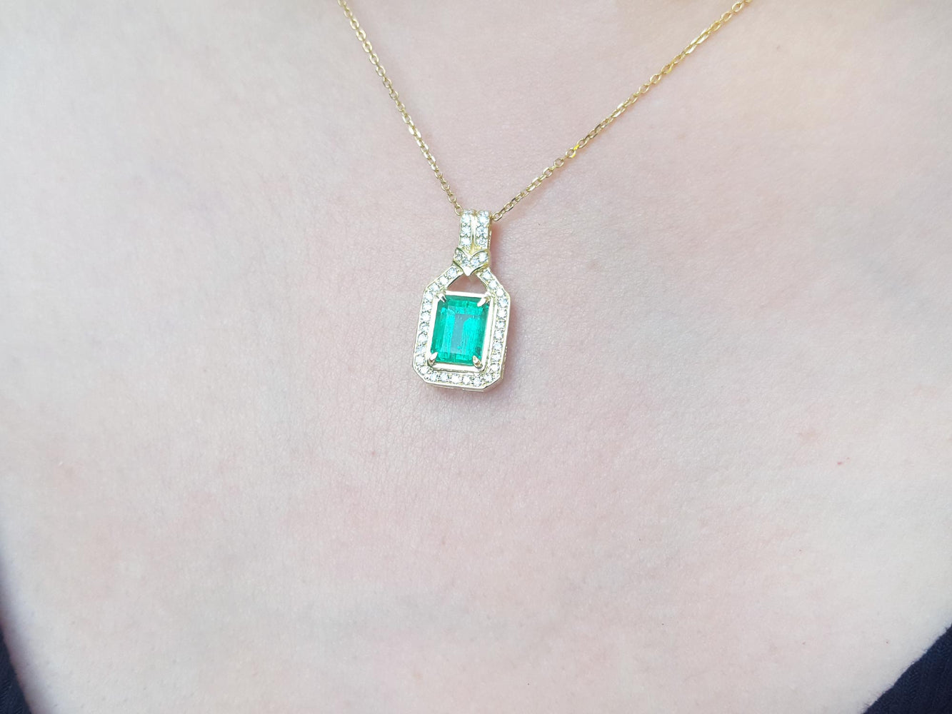 Gold necklace with a pendant featuring a colombian emerald on a light pink background
