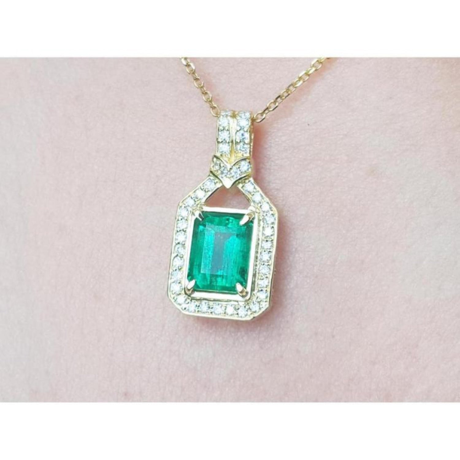 Natural colombian emerald pendant with diamond accents on a gold chain against a pink skin background.