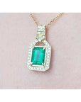 Natural colombian emerald pendant with diamond accents on a gold chain against a pink skin background.