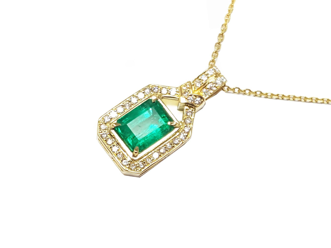 A 18k yellow gold necklace with an emerald and diamond pendant on a white background