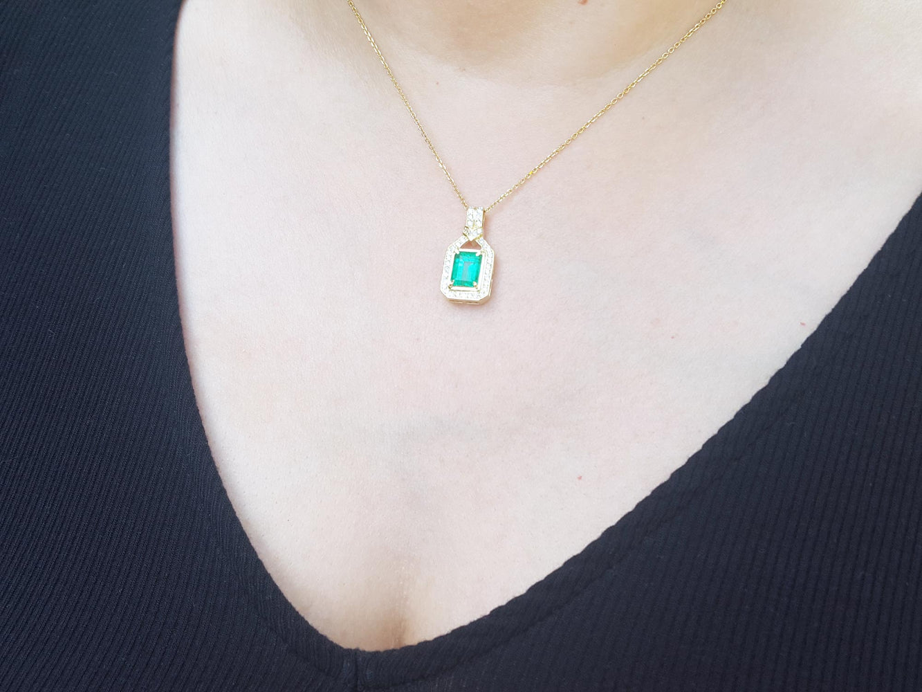 Gold necklace with an emerald-cut emerald pendant on a person wearing a black top.