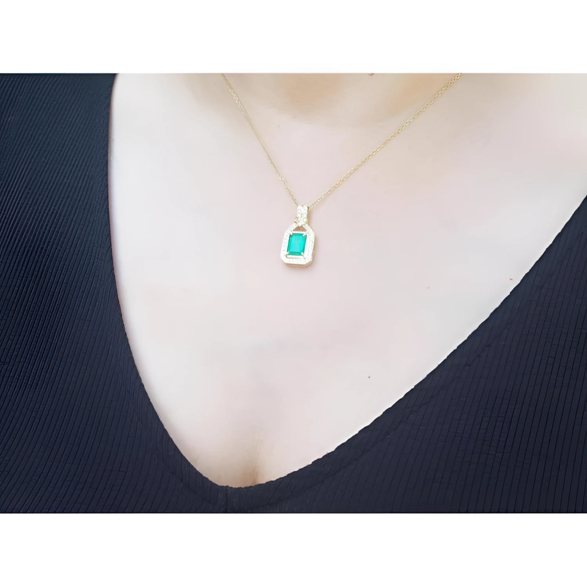 Emerald pendant with natural diamonds on 18K yellow gold chain, worn on a woman's chest.