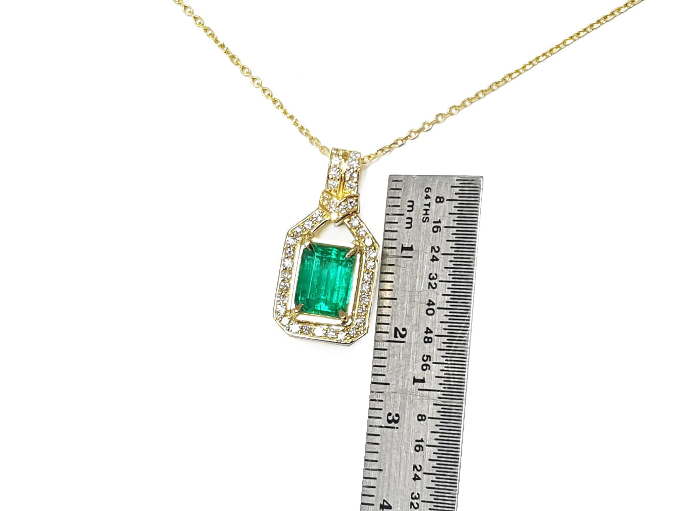 Gold necklace with an emerald pendant next to a ruler for scale on a white background